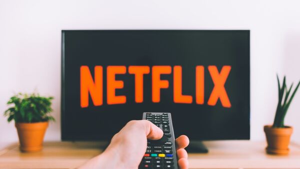 Una persona apunta con el control remoto a una pantalla de televisión con el logotipo de Netflix - Sputnik Mundo
