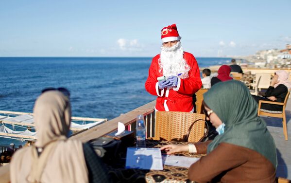 Un hombre palestino vestido de Papá Noel toma un pedido en un café ubicado en la playa en Gaza. - Sputnik Mundo