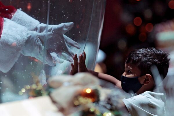 Un niño y Papá Noel con un separador transparente en medio en un centro comercial en Brasilia. - Sputnik Mundo