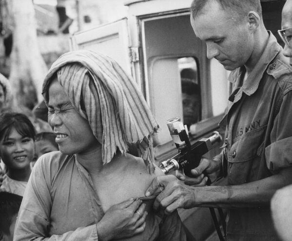 Un médico estadounidense le pone la vacuna contra el cólera a refugiado de una inundación en el Centro de Atención a Refugiados en la montaña Nui Sam, Vietnam, año 1966. - Sputnik Mundo