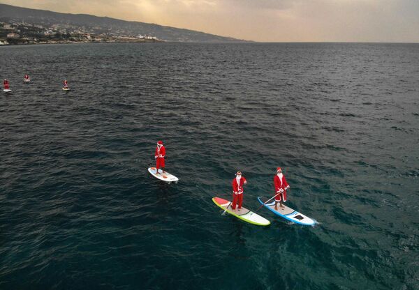 Unos surfistas disfrazados de Santa Claus cerca de la costa mediterránea de Batrún en el norte del Líbano. - Sputnik Mundo