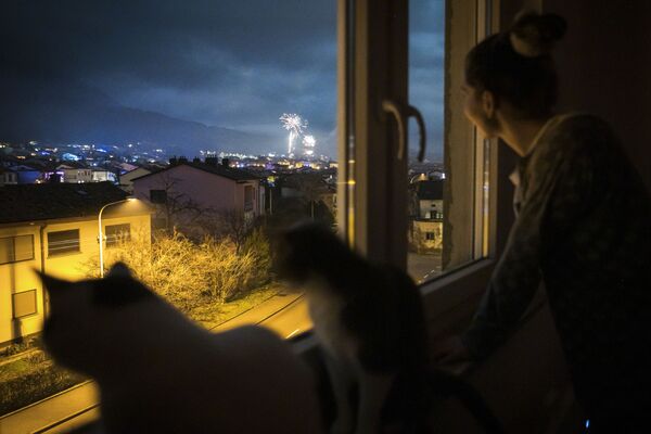 Una mujer y sus gatos miran los fuegos artificiales de las celebraciones de Nochevieja a través de la ventana de su casa en Ajdovscina (Eslovenia). - Sputnik Mundo