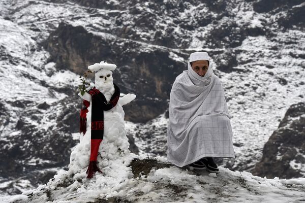 Un hombre se sienta junto a un muñeco de nieve después de las primeras nevadas en Landi Kotal (Pakistán) el 27 de diciembre de 2020. - Sputnik Mundo