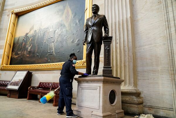 Una empleada del Capitolio limpia una estatua del expresidente Ronald Reagan ubicada en el interior de la Rotonda del Capitolio, un día después de que el edificio fuera invadido. - Sputnik Mundo