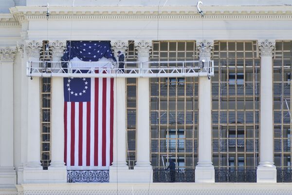 Unos empleados del Capitolio instalan una bandera en el exterior del edificio, mientras se llevan a cabo los preparativos para la toma de posesión del nuevo presidente. - Sputnik Mundo
