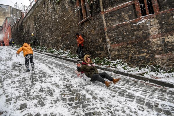 Unos niños se deslizan en una calle de la ciudad de Estambul cubierta de nieve.  - Sputnik Mundo
