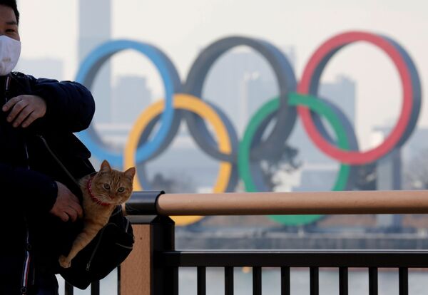 Un hombre con un gato frente a los anillos olímpicos. Los JJOO debían celebrarse del 24 de julio al 9 de agosto de 2020, pero se aplazaron a 2021 debido a la pandemia. Se espera que el importante evento deportivo tenga lugar entre el 23 de julio y el 8 de agosto.  - Sputnik Mundo