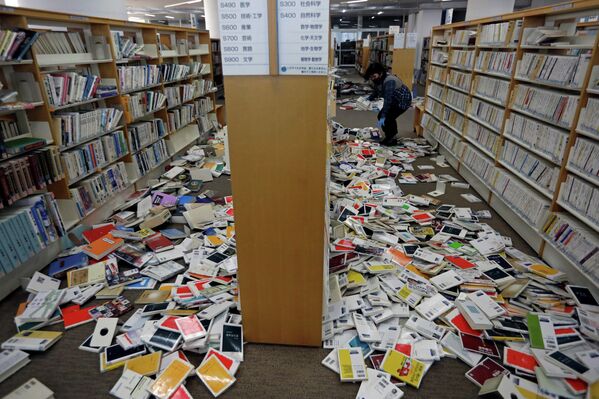 El trabajador de una biblioteca de la ciudad de Iwaki, en Fukushima, intenta recoger los libros después de que cayesen de los estantes. - Sputnik Mundo