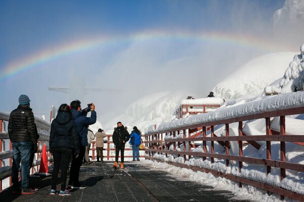 Los visitantes admiran el arcoíris que se formó sobre el agua que corre alrededor del hielo formado debido a bajas temperaturas al pie de las cataratas de Niágara, Nueva York, EEUU.  - Sputnik Mundo