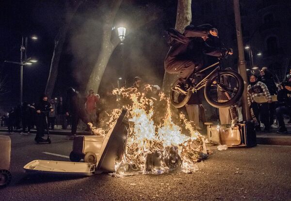 Un ciclista salta sobre los restos de una barricada en llamas tras una manifestación en apoyo al rapero Pablo Hasél en Barcelona, España. - Sputnik Mundo
