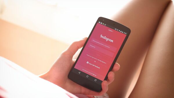 Mujer adolescente sosteniendo un celular con la app Instagram abierta - Sputnik Mundo