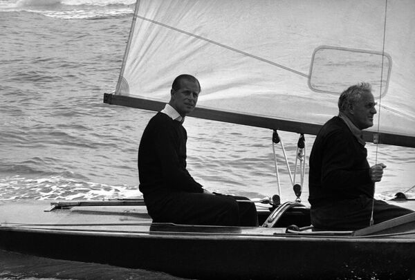 El príncipe Felipe, duque de Edimburgo, al timón del Coweslip, con su compañero de navegación Uffa Fox, antes de la salida de la regata del Royal London Yacht Club, el 6 de agosto de 1963. - Sputnik Mundo