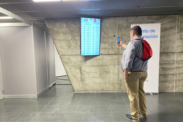 Un hombre dentro del WiZink Center de Madrid fotografía la pantalla donde aparecen los turnos para vacunarse - Sputnik Mundo