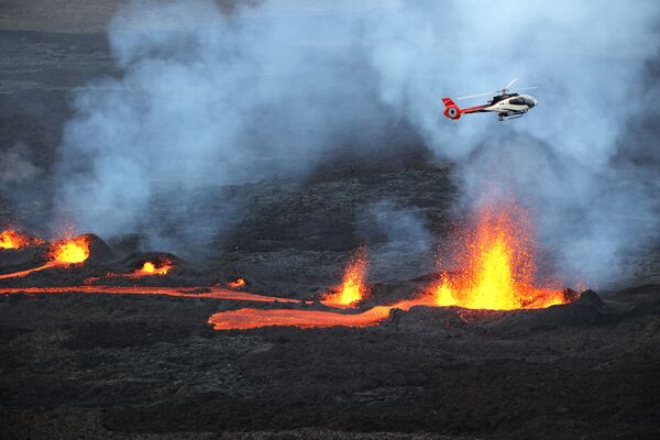 Un helicóptero sobrevuela la lava que fluye desde el volcán Piton de la Fournaise en la isla de Reunión. - Sputnik Mundo