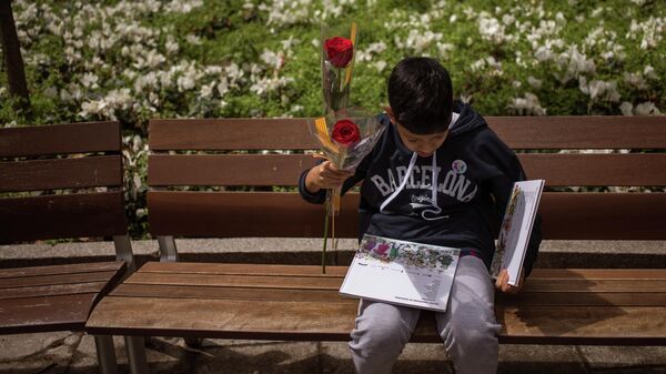 Un chico sostiene una rosa y un par de libros en el Día de Sant Jordi, Barcelona - Sputnik Mundo