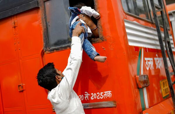Un trabajador migrante pasa a su hijo a través de la ventana de un autobús en Ghaziabad (la India) al regresar a su aldea, después de que el gobierno de Nueva Delhi decretara un cierre de seis días en un intento de contener la propagación del COVID-19. - Sputnik Mundo