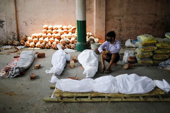 Un hombre está sentado junto a los cuerpos de los muertos por el COVID-19 antes de una cremación masiva en Nueva Delhi. - Sputnik Mundo