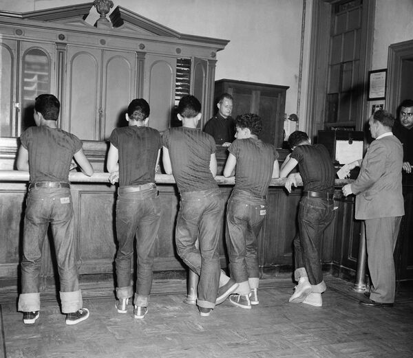 En los años 50, los jeans azules fueron prohibidos en ciertos lugares como escuelas, teatros y restaurantes de Estados Unidos porque eran vistos como una forma de rebelión contra el conformismo.En las fotos: unos jóvenes sospechosos de delincuencia en una comisaría de policía de Nueva York, 1959.  - Sputnik Mundo