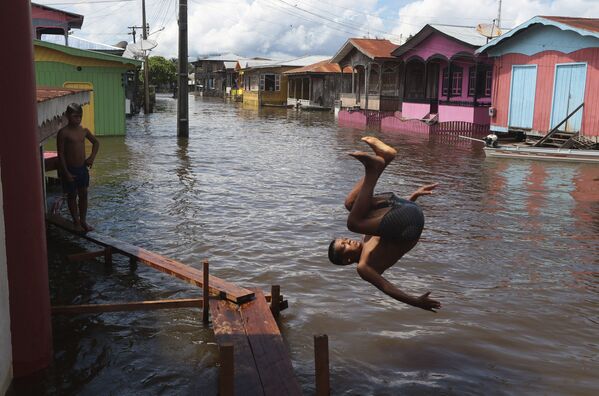 Un chico salta al agua en una calle inundada en el estado de Amazonas (Brasil).  - Sputnik Mundo