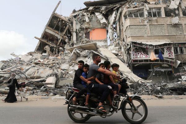 Unos palestinos pasan por el lugar de uno de los ataques aéreos israelíes en Gaza. - Sputnik Mundo