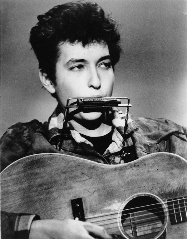 Al igual que otros adolescentes de su generación, el joven Bob Dylan era un gran aficionado al rock&#x27;n&#x27;roll y tocó &#x27;covers&#x27; de los éxitos de Elvis Presley y Little Richard junto a los compañeros de su grupo musical que formó en el colegio. En la foto: Bob Dylan toca la armónica y la guitarra en un club de EEUU, en 1963. - Sputnik Mundo