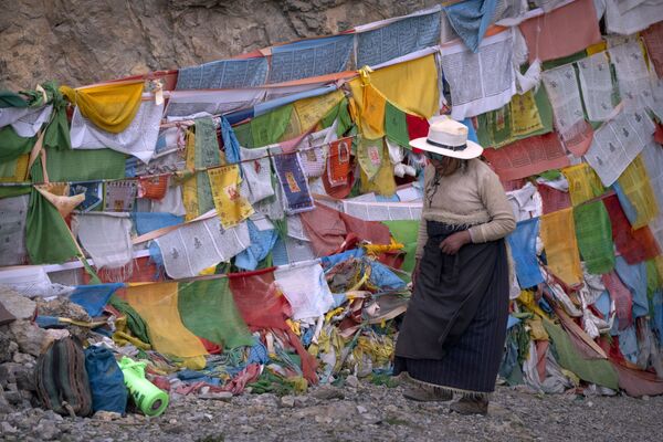 Una mujer tibetana pasa junto a banderas de oración en un santuario budista en Namtso, en la Región Autónoma del Tíbet (China). - Sputnik Mundo