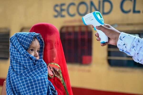 Un trabajador sanitario le toma la temperatura a una pasajera con un bebé en una estación de tren de Bombay, la India. - Sputnik Mundo