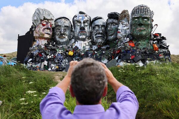 Un hombre fotografía una escultura hecha con residuos tecnológicos, denominada &#x27;Mount Recyclemore&#x27;, instalada en vísperas de la cumbre del G7 en Hayle Towans, Reino Unido. - Sputnik Mundo