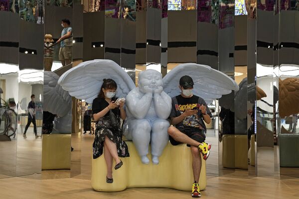 Dos visitantes observan sus teléfonos mientras permanecen junto a la escultura de un ángel en un centro comercial de Pekín, China. - Sputnik Mundo
