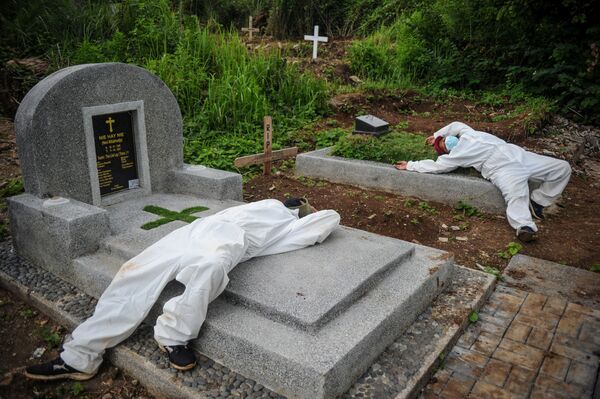 Dos hombres que trabajan sepultando personas en un cementerio descansan tras los masivos entierros por el COVID-19 en Bandung, Indonesia. - Sputnik Mundo