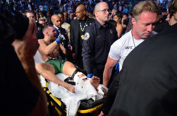 El luchador irlandés Conor McGregor abandona el octágono en camilla tras fracturarse la pierna en su pelea contra Dustin Poirier en el torneo UFC 264. - Sputnik Mundo