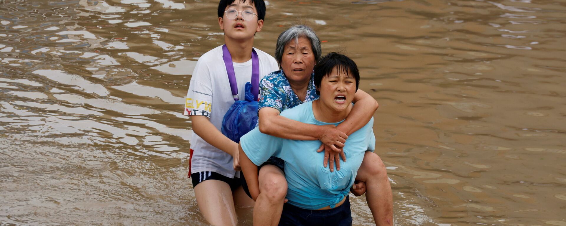 Женщина несет пожилую женщину  через паводковые воды после проливного дождя в Чжэнчжоу, провинция Хэнань, Китай - Sputnik Mundo, 1920, 26.07.2021