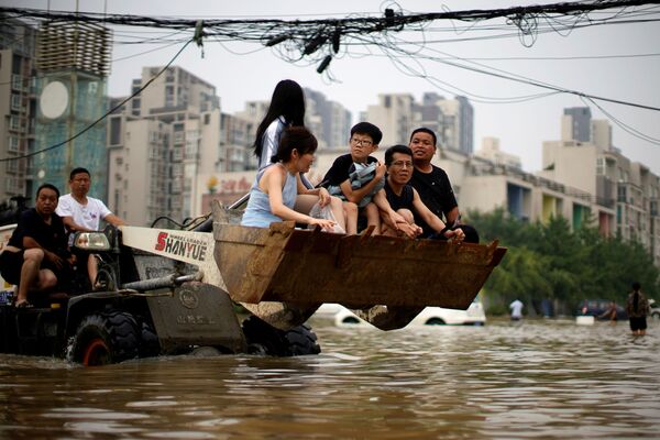Residentes locales se mueven en una carretilla elevadora a través de un área inundada en Zhengzhou. - Sputnik Mundo