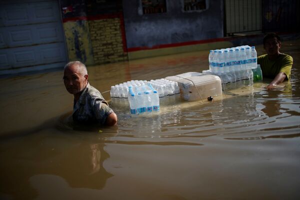 La gente traslada agua potable a través de un área inundada en Xinxiang. - Sputnik Mundo
