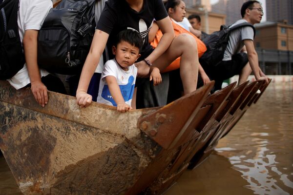Los residentes locales se mueven en una carretilla elevadora a través de un área inundada en Zhengzhou. - Sputnik Mundo