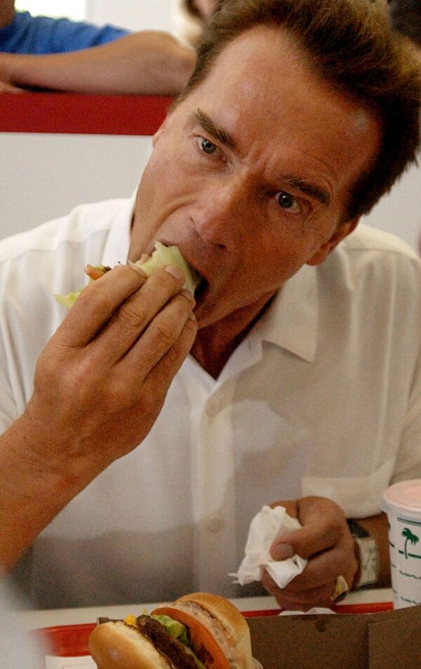 La hamburguesa inició su camino hacia la fama en 1904, tras la Feria Mundial de San Luis (en Missouri). En la foto, el gobernador de California Arnold Schwarzenegger se come una hamburguesa envuelta en lechuga en el In-N-Out Burger de Merced de California en 2003. - Sputnik Mundo