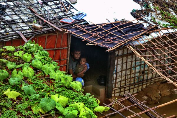 Un refugiado rohinyá y su hijo miran hacia afuera desde el interior de su refugio inundado tras las fuertes lluvias que azotaron el campo de refugiados de Kutupalong (Bangladés). - Sputnik Mundo