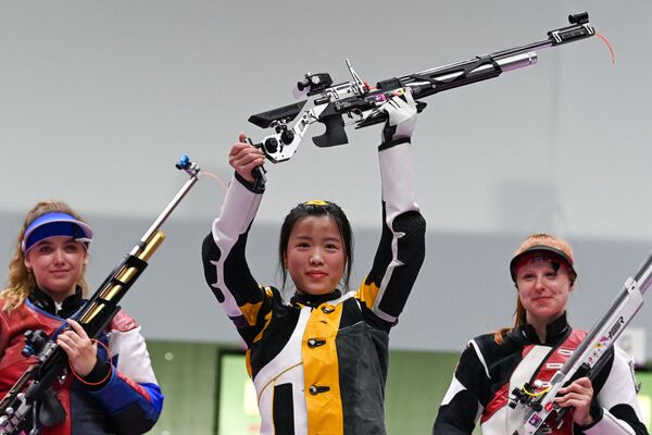 La atleta china Yang Qian celebra su victoria en el podio, entre la rusa Anastasiya Galashina y la suiza Nina Christen, tras ganar en la final de rifle de aire femenino de 10 metros el 24 de julio de 2021. - Sputnik Mundo