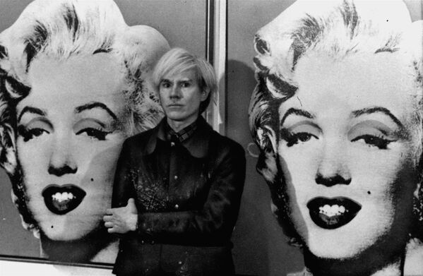 El año siguiente, pasó a utilizar la técnica de serigrafía fotográfica para producir en masa estas imágenes deliberadamente banales de bienes de consumo. A la vez, comenzó a imprimir numerosas variaciones de retratos de celebridades en colores llamativos, siendo su representación de Marylin Monroe quizás el más conocido de ellos.En la foto: Andy Warhol posa delante del retrato de la fallecida actriz Marilyn Monroe, en la Galería Tate de Londres, el 15 de febrero de 1971. - Sputnik Mundo