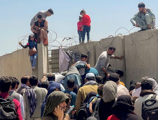 Un hombre agarra a una chica para entrar en el aeropuerto internacional Hamid Karzai en Kabul, Afganistán, el 16 de agosto de 2021. Es el único punto desde donde miles de afganos pueden abandonar su país. Los militares estadounidenses lo custodian. - Sputnik Mundo