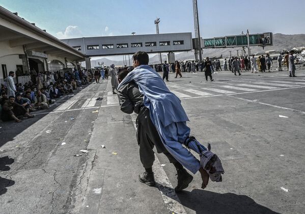 Un voluntario transporta a un hombre herido mientras otras personas esperan en el aeropuerto de Kabul el 16 de agosto de 2021. - Sputnik Mundo