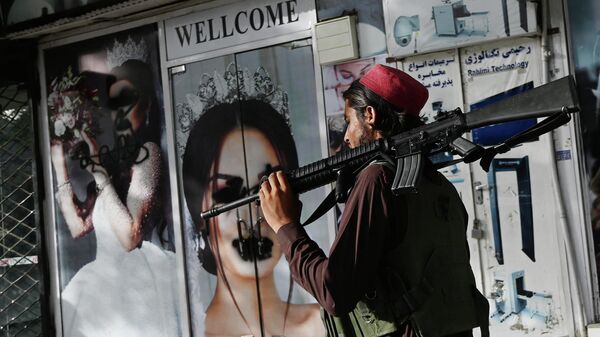 Un soldado talibán camina frente a un salón de belleza con imágenes de mujeres desfiguradas con spray, en Shar-e-Naw en Kabul, el 18 de agosto de 2021 - Sputnik Mundo
