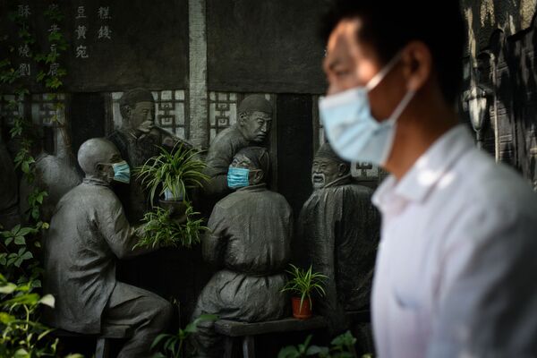 Un hombre pasa cerca de una escultura cubierta con mascarillas en el exterior de un restaurante en un callejón en Pekín, el 29 de agosto de 2021. - Sputnik Mundo