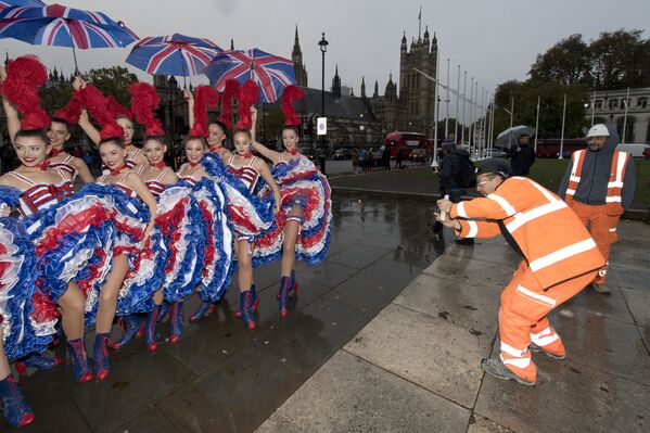 Un obrero toma una foto de un grupo de bailarinas del Moulin Rouge en el centro de Londres. - Sputnik Mundo