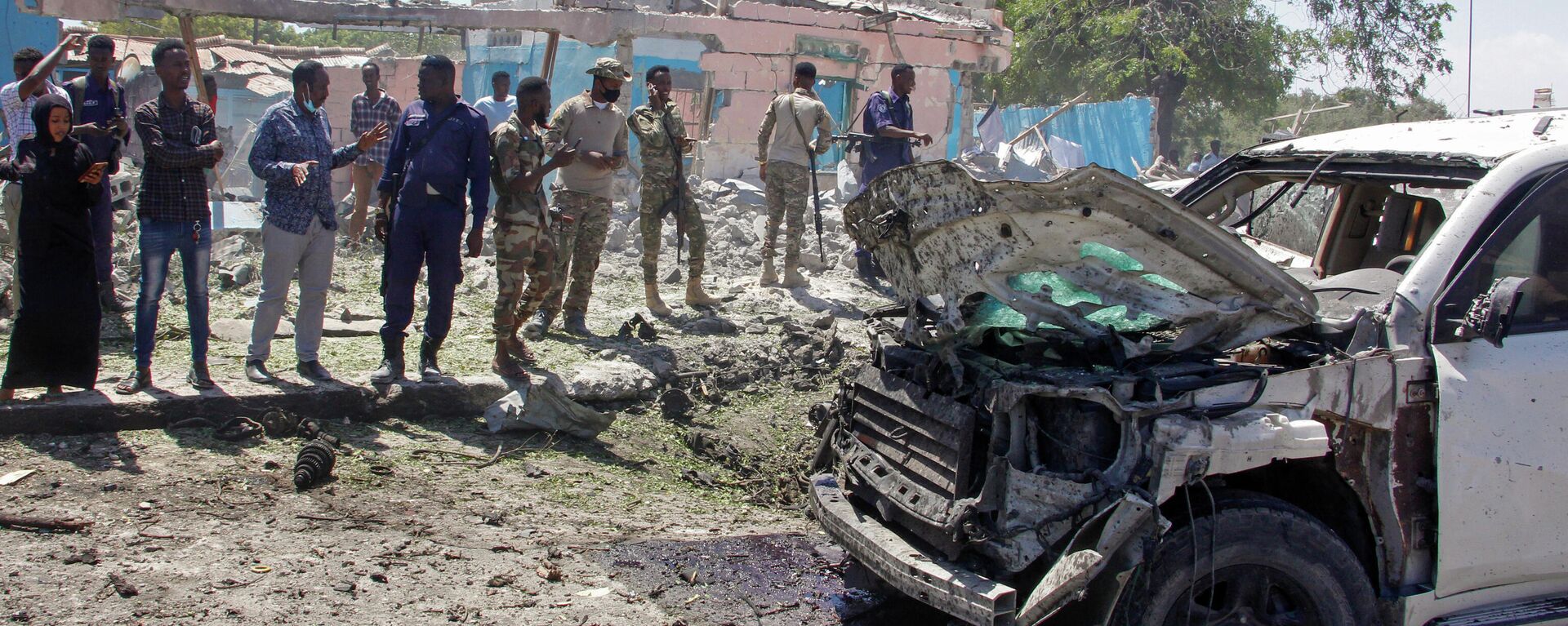 Fuerzas de seguridad y otras personas observan los restos de un vehículo blindado alcanzado por una explosión en Mogadiscio, Somalia, el 12 de enero de 2022. - Sputnik Mundo, 1920, 12.01.2022