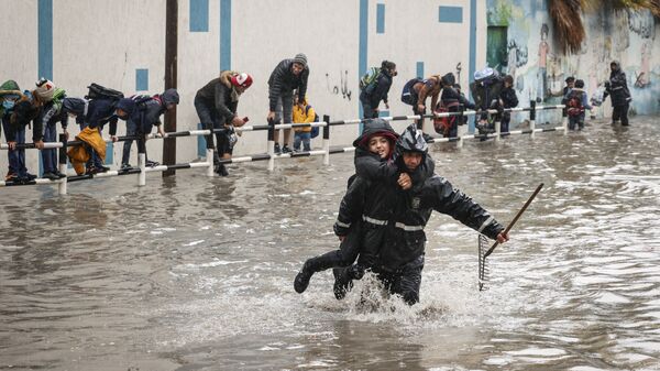 Муниципальный работник переносит школьника на другой край улицы во время ливневых затоплений в Газе - Sputnik Mundo
