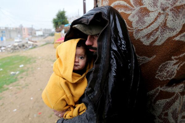 Un hombre con un bebé bajo la lluvia lluvia en Khan Younis, en el sur de la Franja de Gaza. - Sputnik Mundo