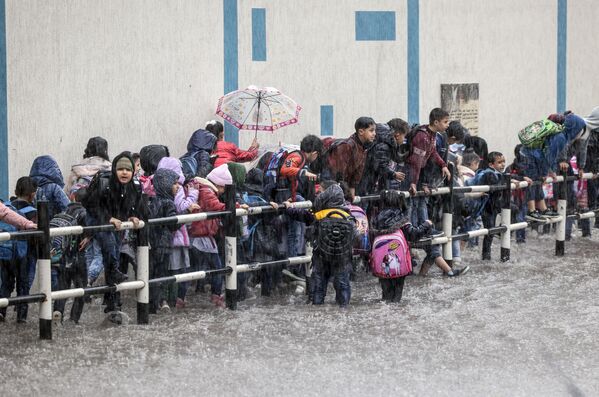 Varios estudiantes palestinos esperan su turno para cruzar una calle inundada en la ciudad de Gaza. - Sputnik Mundo