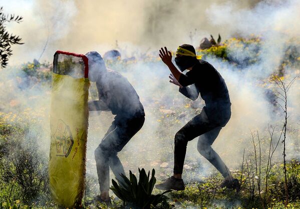Dos jóvenes palestinos se defienden con escudos improvisados mientras las fuerzas de seguridad israelíes dispersan una manifestación contra la apropiación de tierras por parte de Israel en la aldea palestina de Kfar Qaddum, en Cisjordania. - Sputnik Mundo
