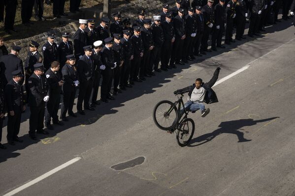 Un ciclista pasa por un cortejo fúnebre tras el funeral de tres bomberos fallecidos en la ciudad de Baltimore (EEUU). - Sputnik Mundo